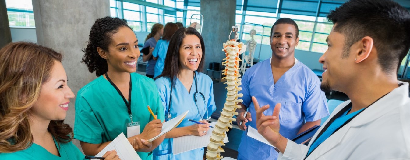 A group of people in scrubs smile and talk next to a model of a spine.